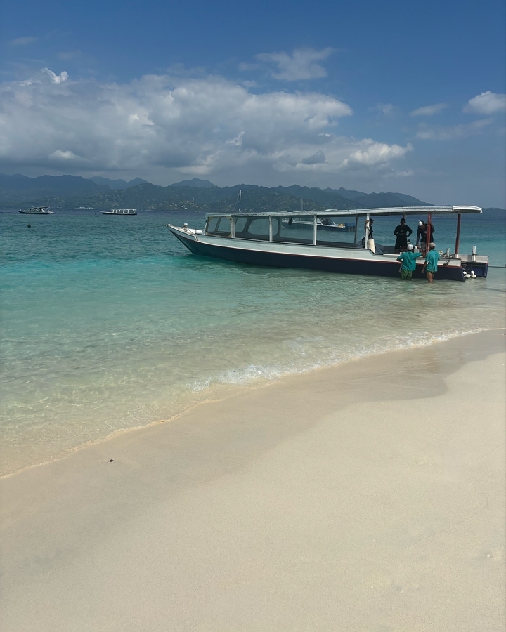 Bateau sur une plage turquoise claire avec des personnes à proximité.