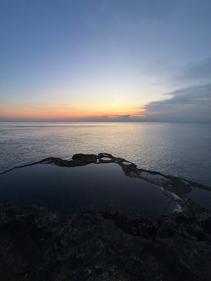 Vue du coucher de soleil sur l'océan avec un affleurement rocheux.