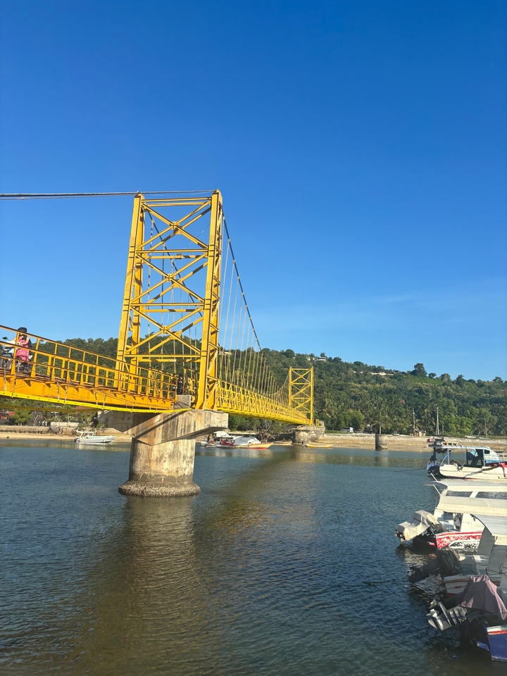 Pont suspendu jaune au-dessus d'une rivière avec des collines au loin.