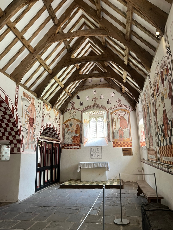 Intérieur d'une chapelle avec des fresques médiévales colorées et un plafond en bois.