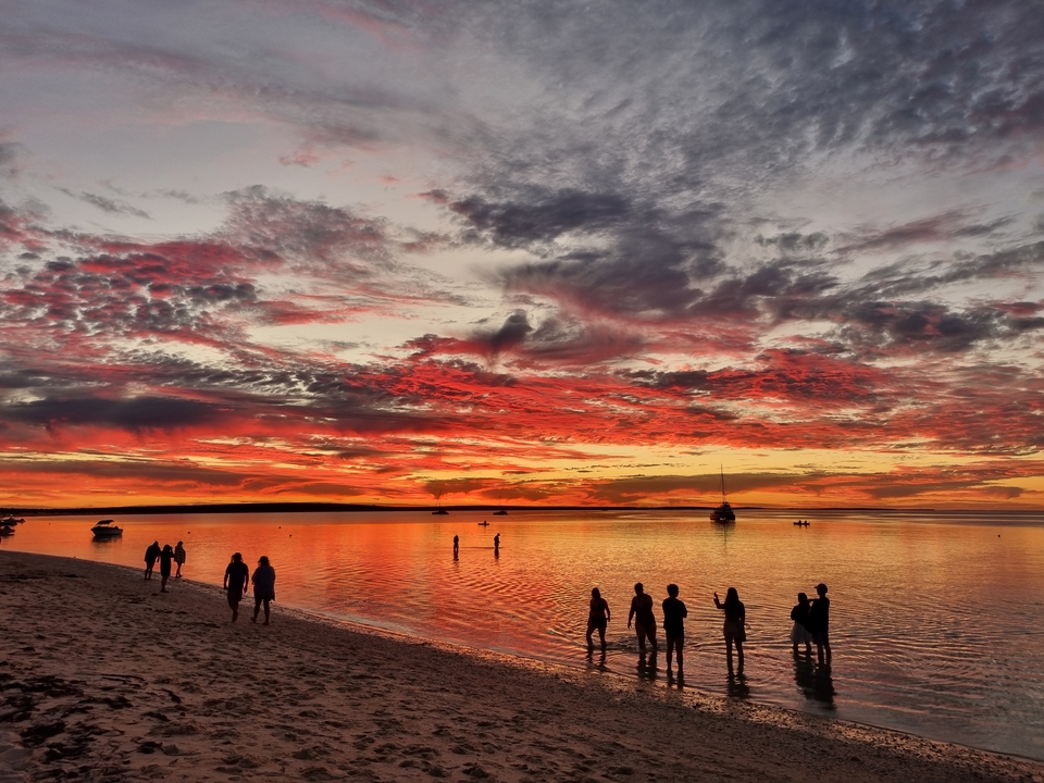 Des gens profitant d'un coucher de soleil éclatant au bord de la mer avec un ciel spectaculaire rempli de nuages colorés.