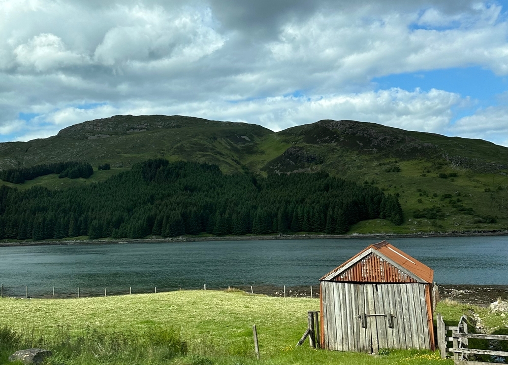Barn by a lake with hills in the background.