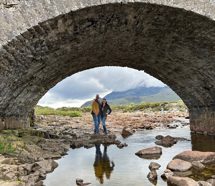 Couple standing under a stone bridge.