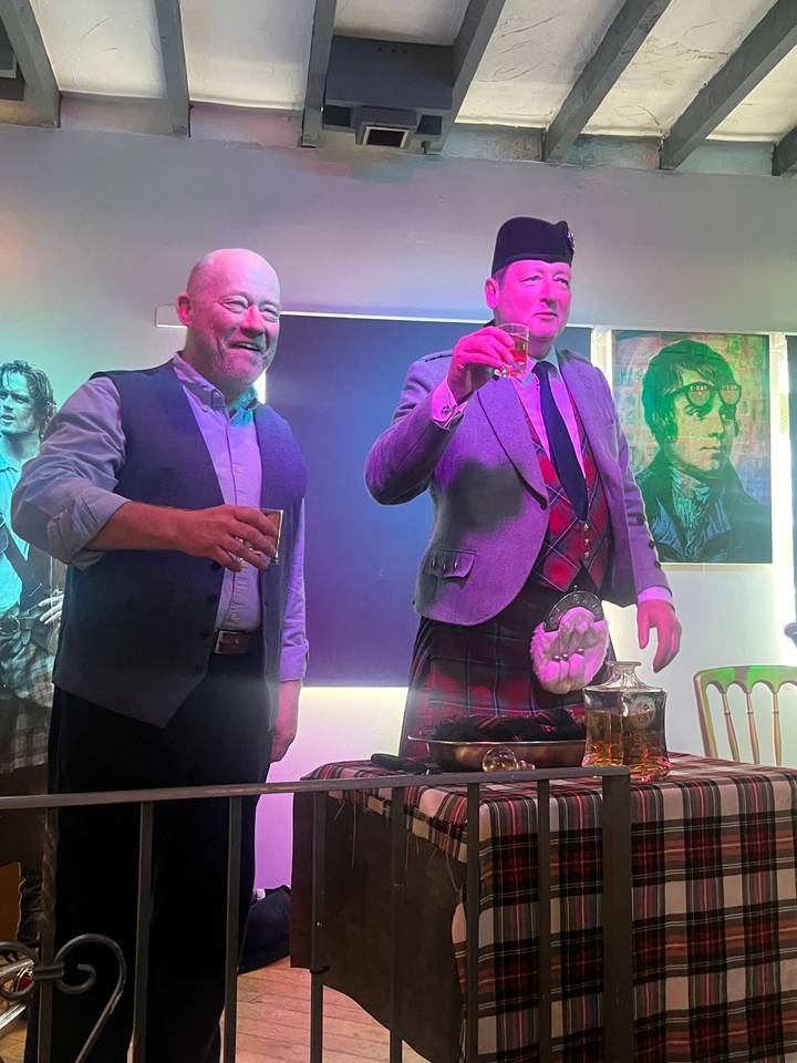 Deux hommes en tenue traditionnelle tenant des boissons à l'intérieur d'un pub.