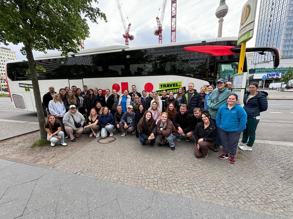 Grand groupe devant un autocar de tourisme dans un environnement urbain.