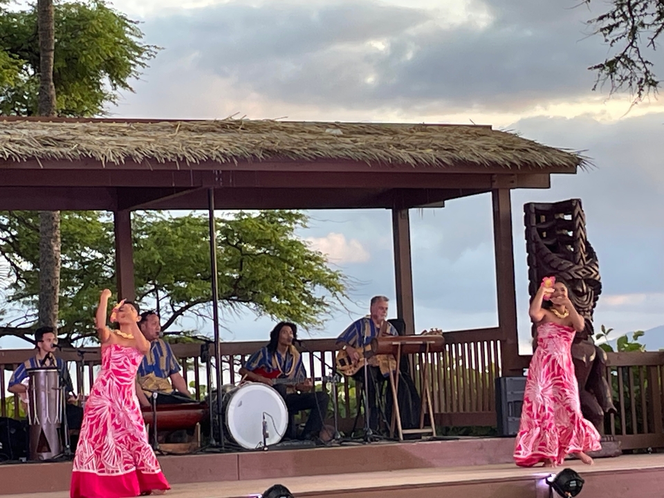 Danseuses de hula se produisant avec des musiciens sous un toit de chaume.