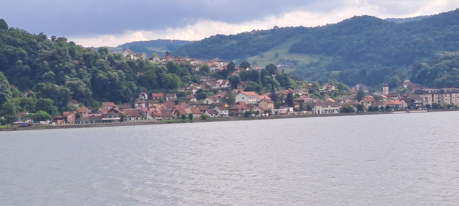 Une vue pittoresque d'un village au bord d'une rivière avec des collines en arrière-plan.