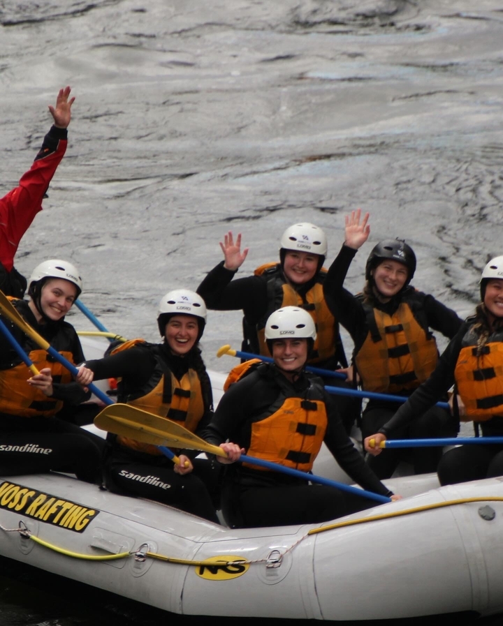 Groupe de personnes qui saluent de la main sur un bateau de rafting.