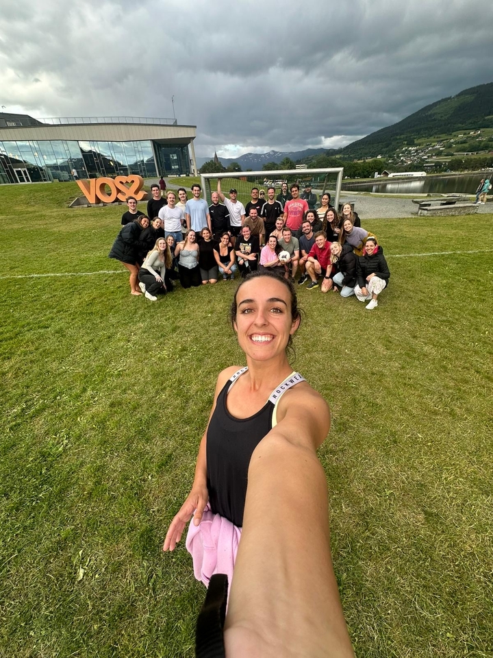 Selfie d'une femme avec un groupe jouant au sport en arrière-plan.