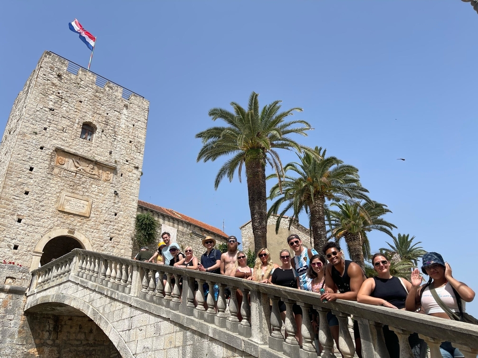 Groupe de personnes sur un escalier en pierre avec une tour historique en pierre et des palmiers.