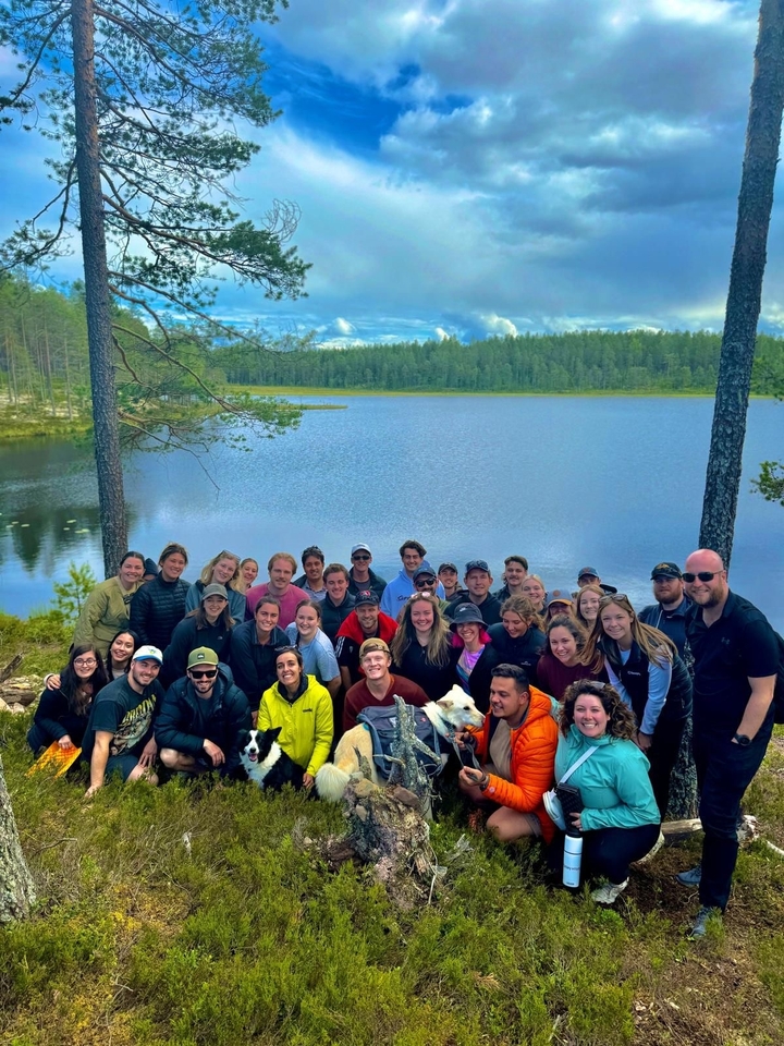 Groupe de personnes posant avec un lac et une forêt en arrière-plan.
