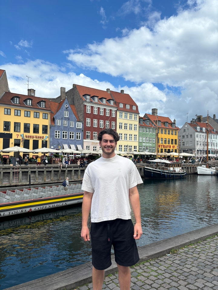 Homme posant devant des bâtiments colorés au bord de l'eau.