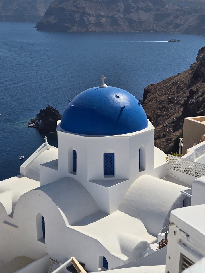 Église au dôme bleu avec vue sur la mer et la côte rocheuse.