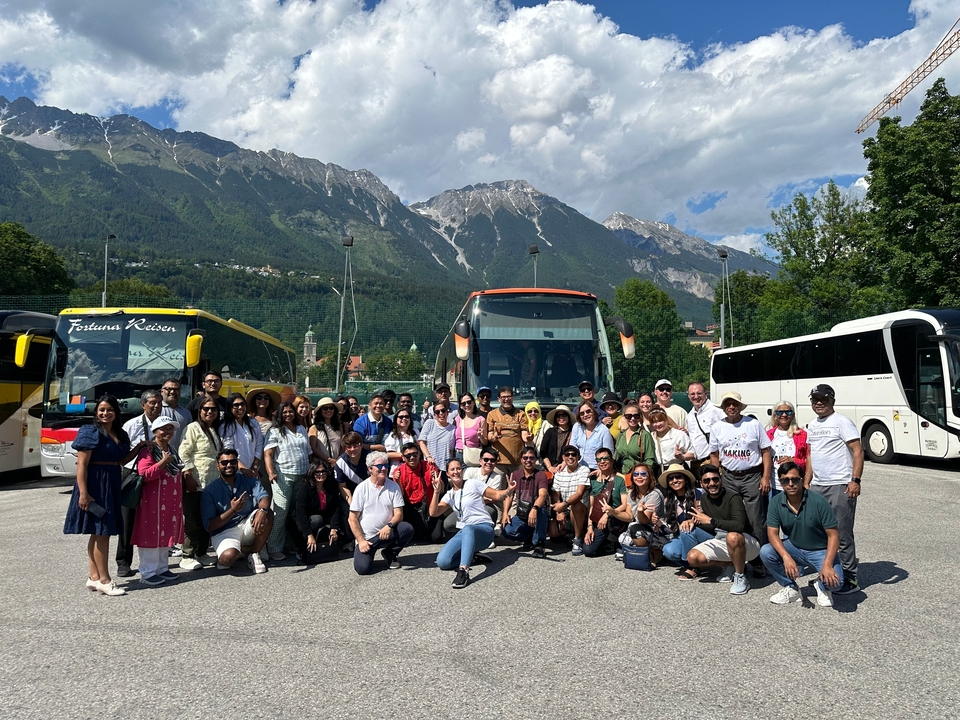 Grand groupe posant devant des autocars de tourisme avec des montagnes en arrière-plan.