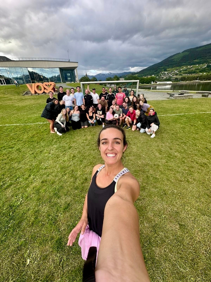 Grand groupe de personnes posant sur l'herbe avec un arrière-plan pittoresque.