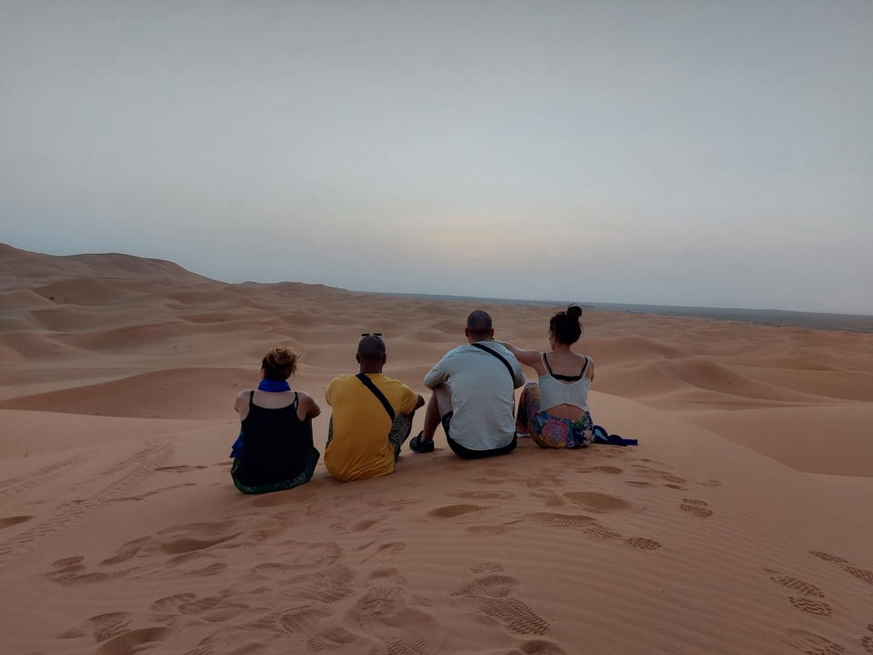 Quatre personnes assises sur des dunes de sable dans un désert, regardant l'horizon.