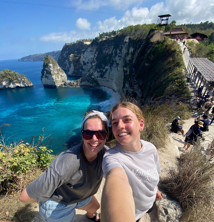 Two friends posing with coastal cliffs in the background.