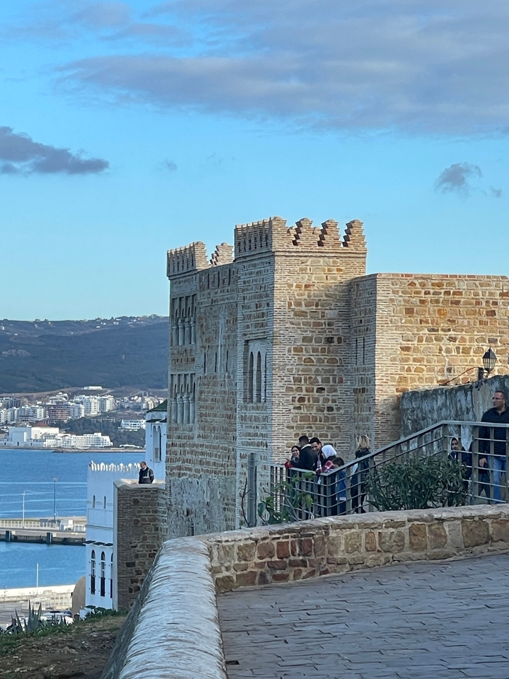 Bâtiment en pierre près d'un front de mer avec des personnes au premier plan.