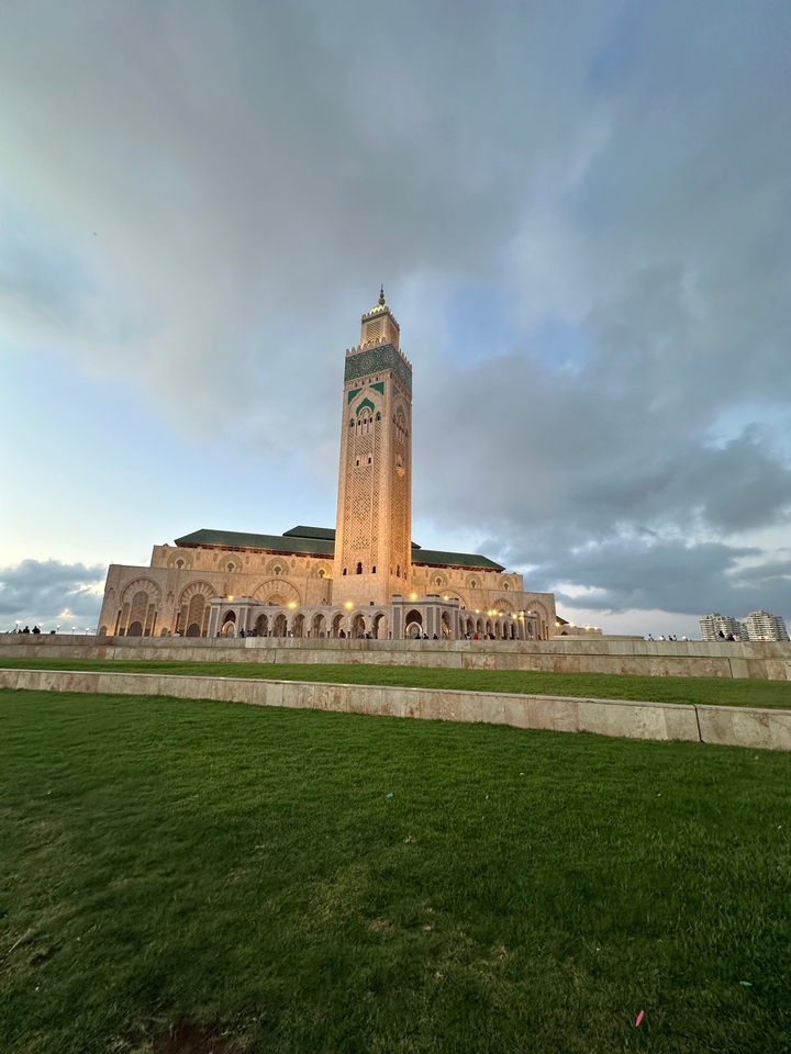 Une mosquée impressionnante avec des gens qui se promènent autour, sous un ciel nuageux.