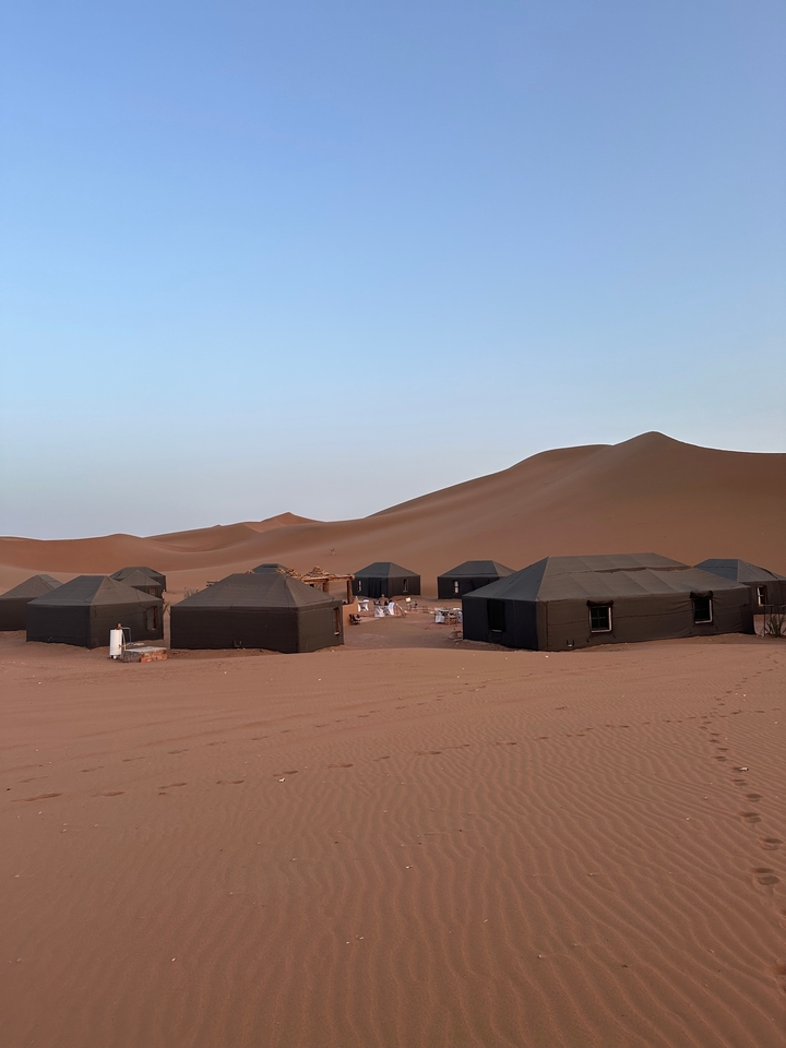 Campement dans le désert avec des tentes et des dunes de sable sous un ciel bleu dégagé.