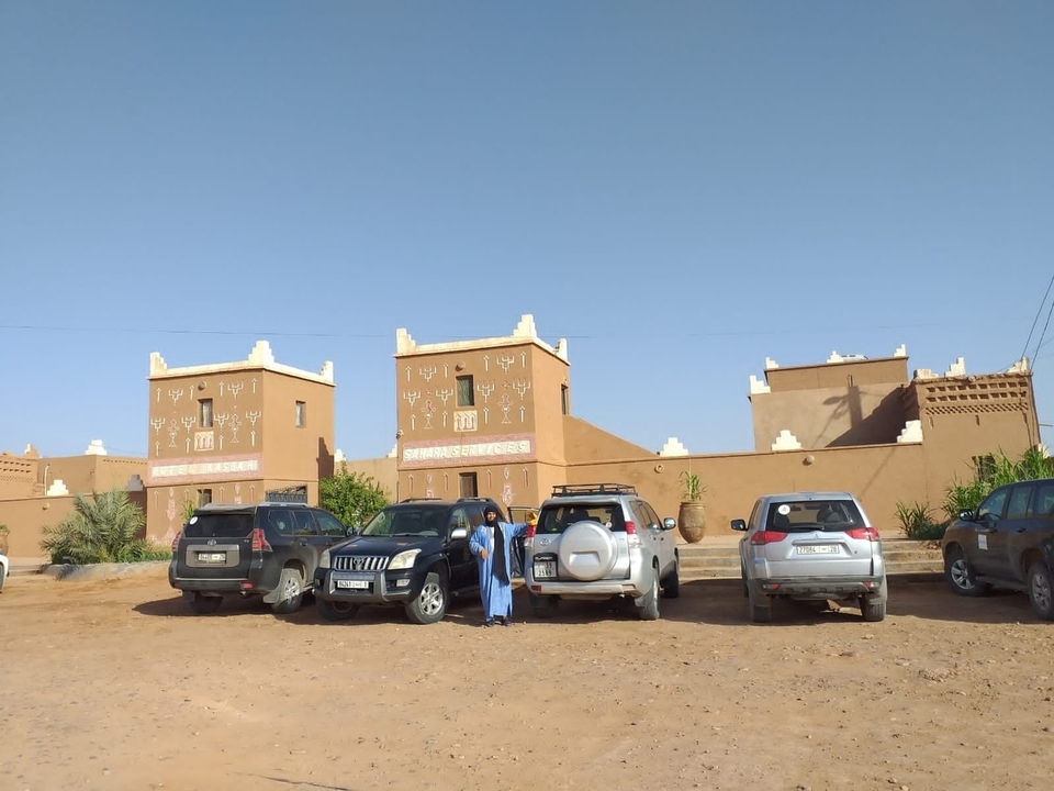 Des gens debout à côté de voitures garées dans un parking.