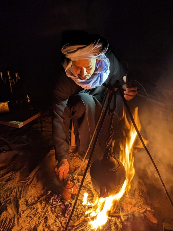 Personne en tenue traditionnelle préparant un feu la nuit.