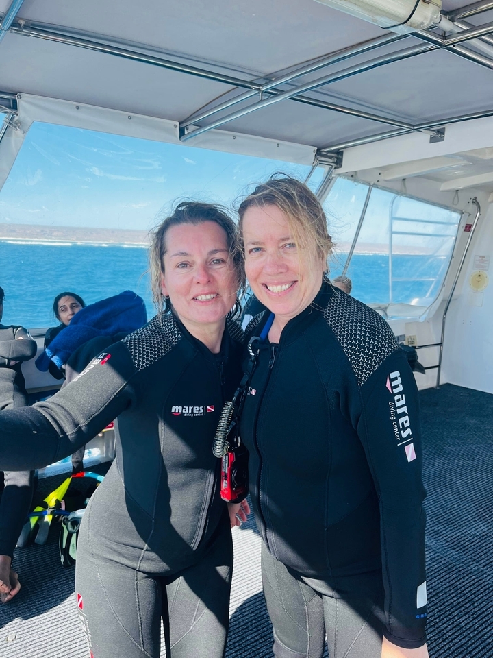Deux femmes en combinaisons de plongée souriantes sur un bateau.