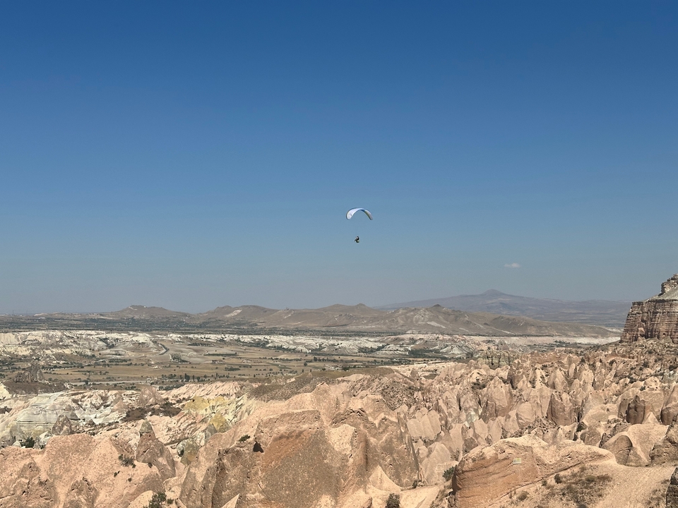 Parapentiste planant au-dessus d'un paysage rocheux sous un ciel dégagé.
