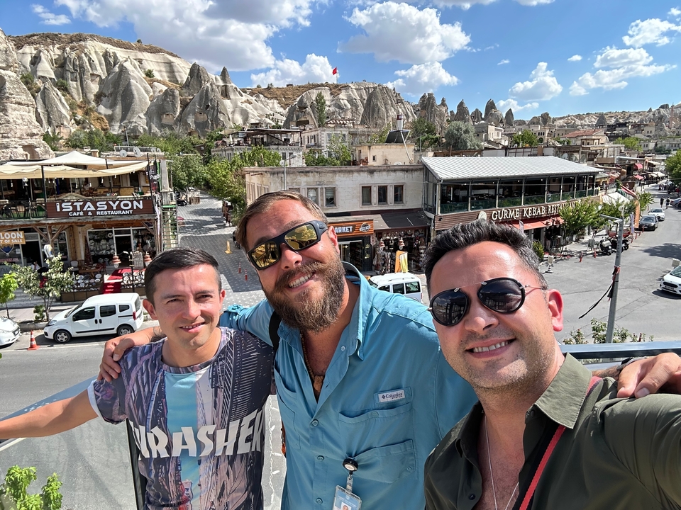 Trois hommes souriants avec des collines rocheuses en arrière-plan.
