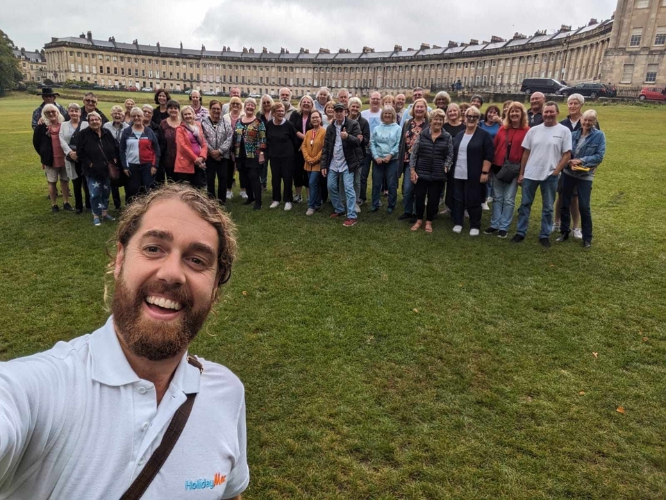 Groupe de personnes posant avec un champ d'herbe et un grand bâtiment derrière.