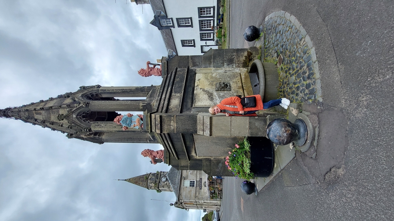 Une personne debout à côté d'une structure architecturale ornée dans une zone pavée de galets.