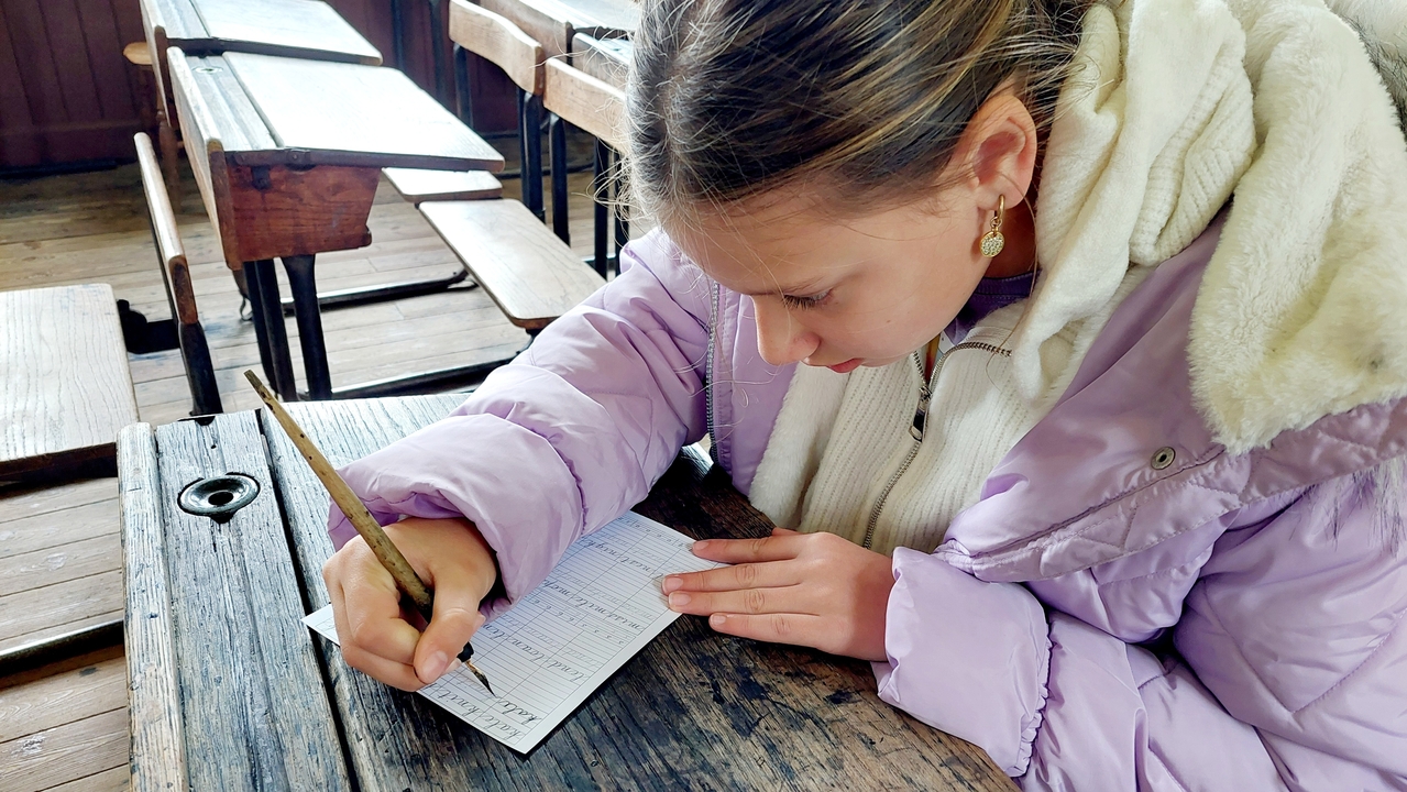 Une personne écrivant à un bureau en bois dans un cadre de salle de classe historique.