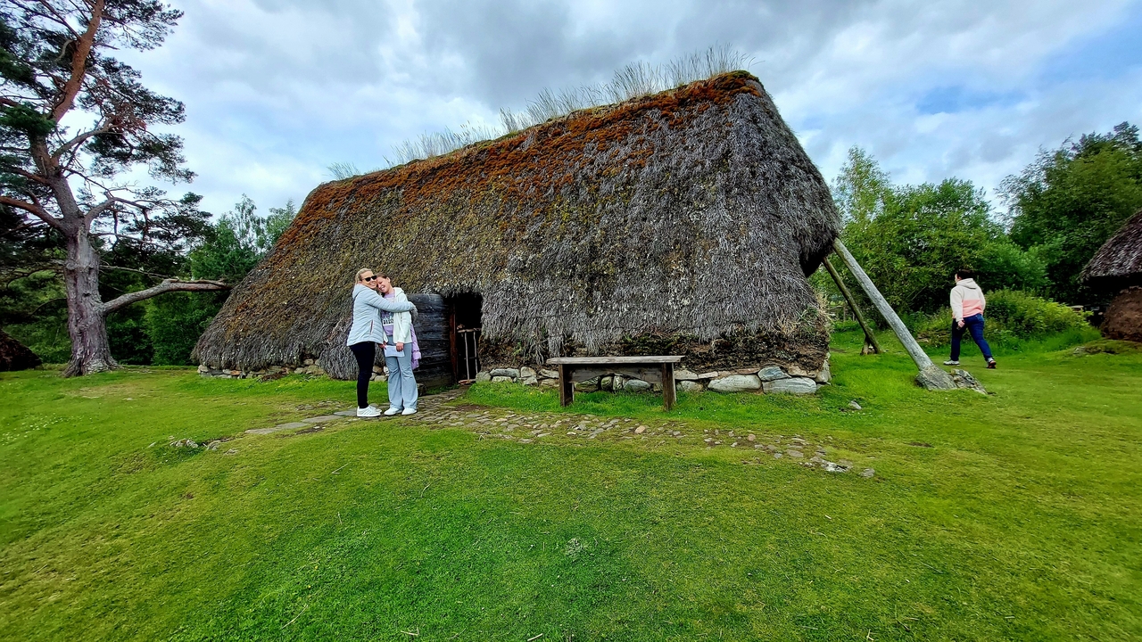 Deux personnes debout joyeusement devant une maison traditionnelle au toit de chaume.