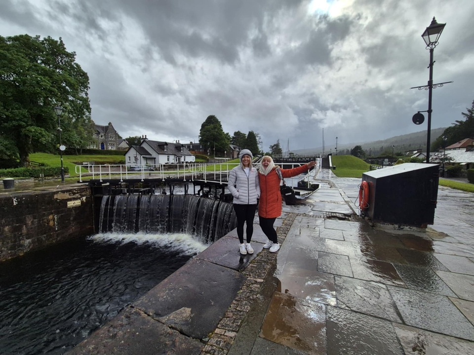 Deux personnes posant et souriant près d'une écluse de canal avec des bâtiments en arrière-plan.