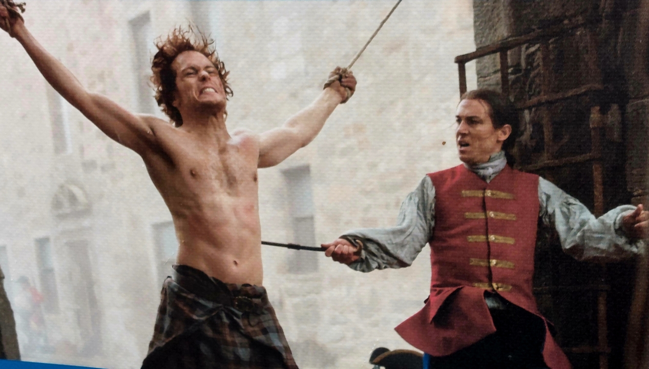 Deux hommes en costumes historiques, l'un attaché et l'autre faisant semblant d'attaquer.