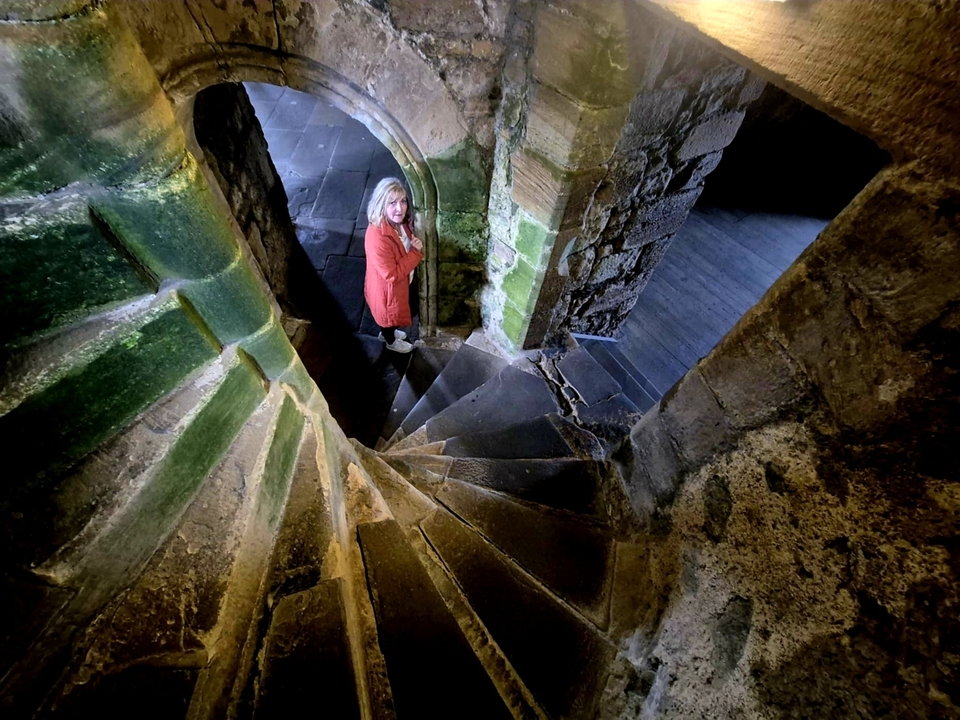 Une personne descendant un escalier en colimaçon en pierre dans un bâtiment historique faiblement éclairé.