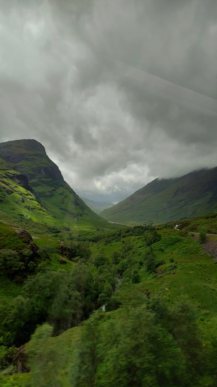 Un paysage pittoresque et nuageux avec une route sinueuse dans une vallée verdoyante entre des collines.