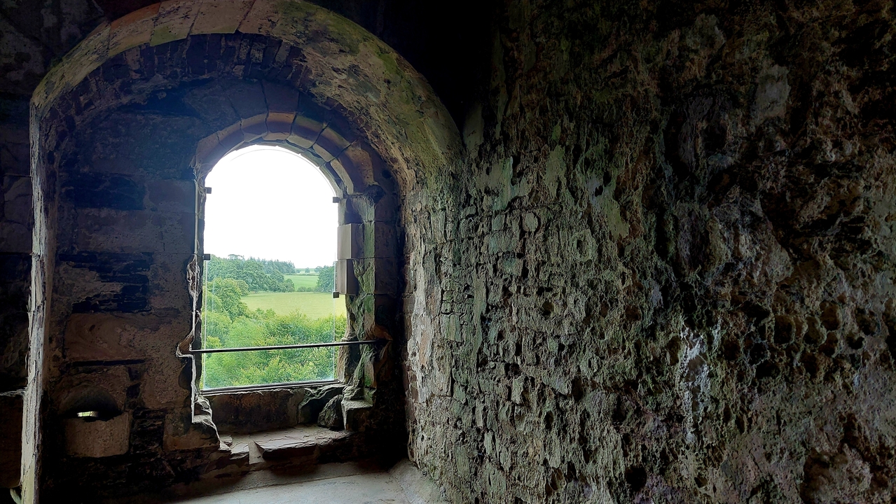 Une vue à travers une fenêtre de pierre d'un paysage verdoyant depuis un ancien bâtiment de pierre.