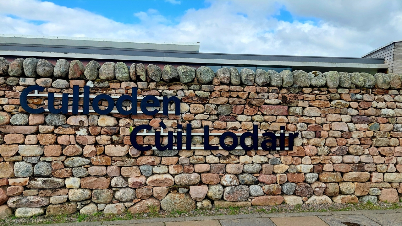 Un panneau indiquant 'Culloden' en anglais et en gaélique écossais sur un mur de pierre.