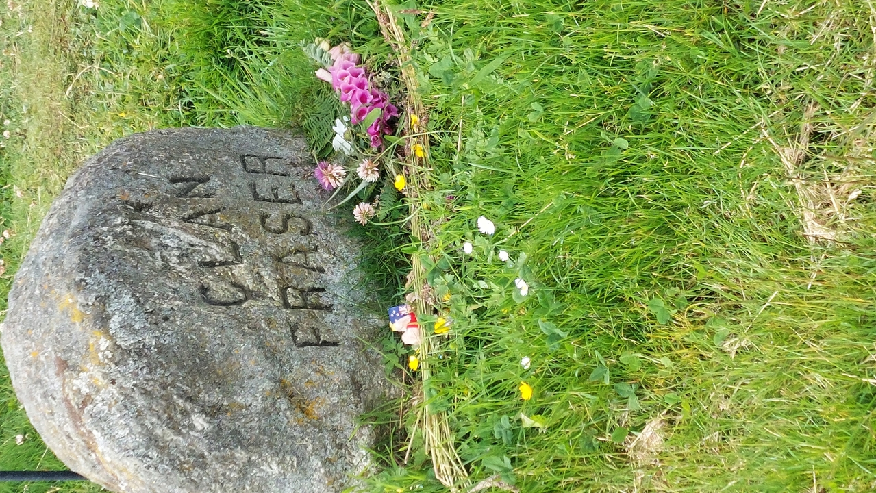 Une pierre marquée 'Clan Fraser' avec des fleurs déposées autour sur une zone herbeuse.