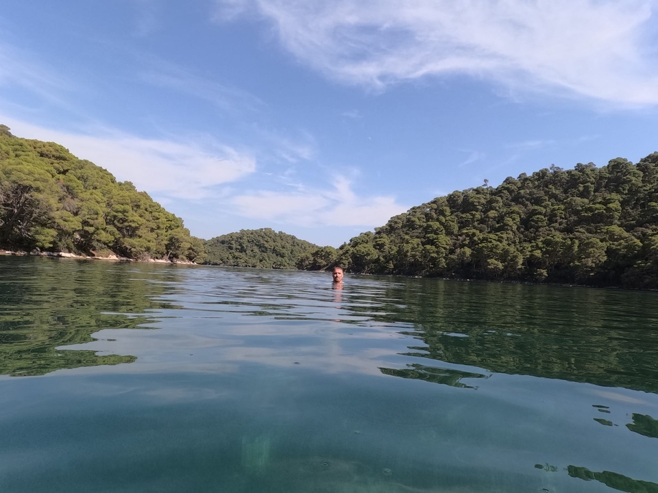 Person swimming in clear water surrounded by green hills.