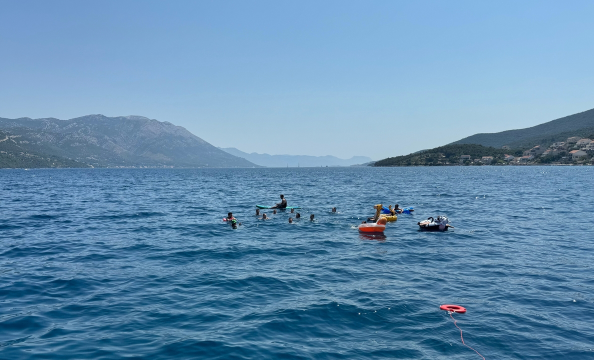 Group of people swimming in the sea with mountains in the background.