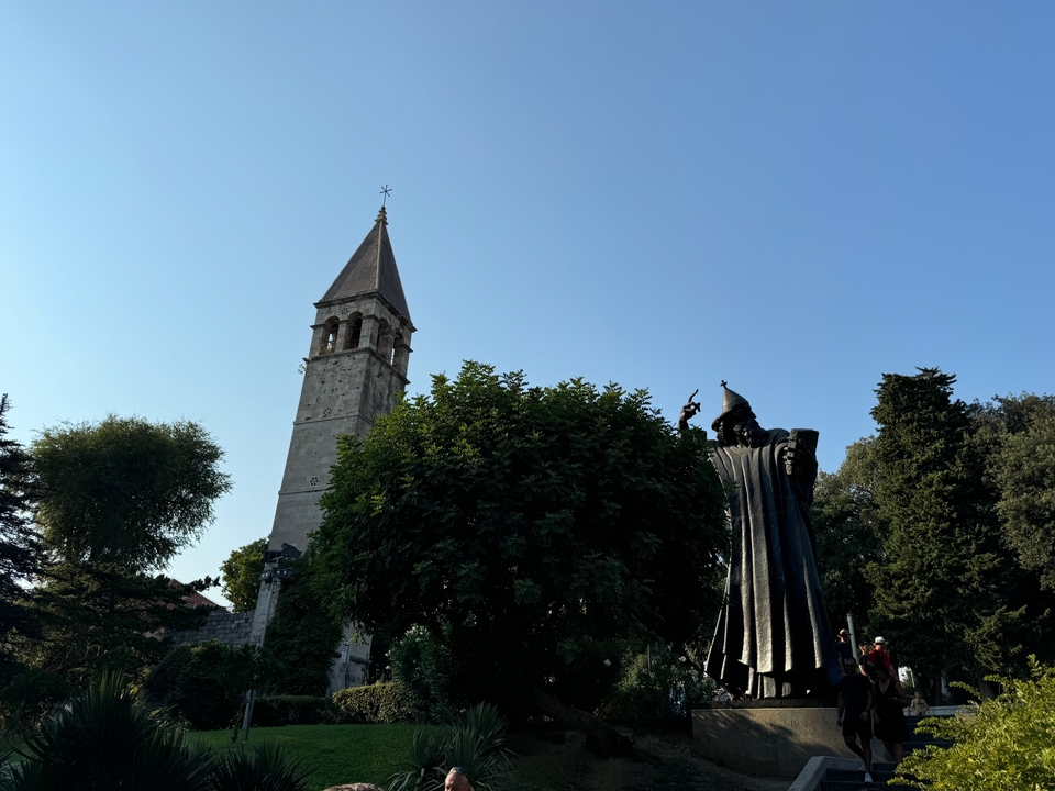 Statue and bell tower with trees and clear sky.