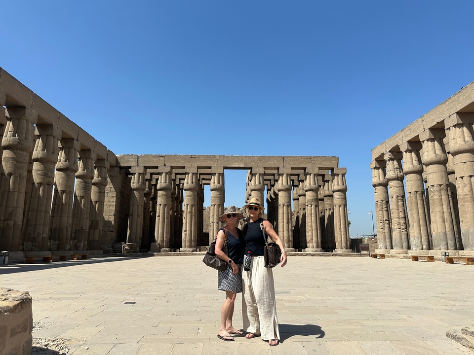 Deux femmes debout devant d'énormes colonnes égyptiennes antiques sous un ciel dégagé.