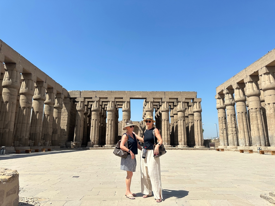 Deux femmes debout devant d'énormes colonnes égyptiennes antiques sous un ciel dégagé.