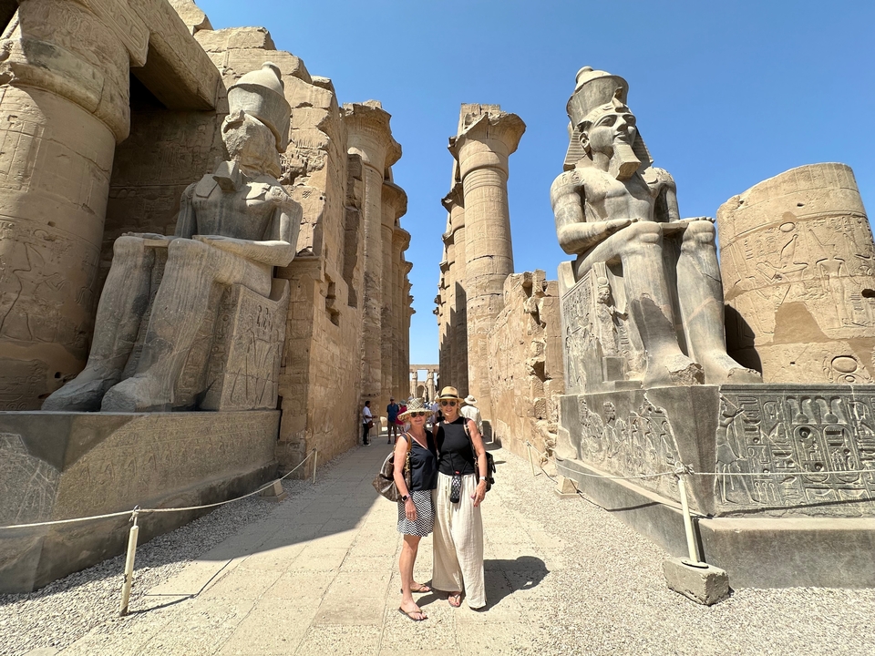 Deux femmes posant entre d'imposantes statues et colonnes de l'Égypte antique.
