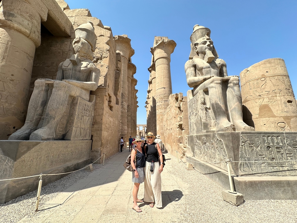 Deux femmes posant entre d'imposantes statues et colonnes de l'Égypte antique.