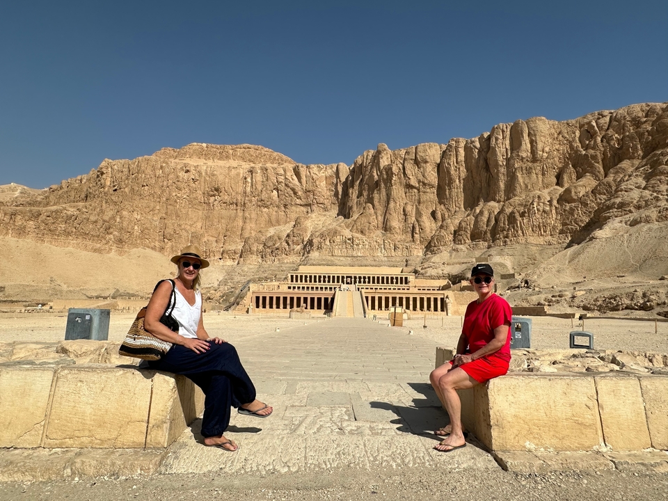 Deux personnes assises devant le temple funéraire d'Hatchepsout avec des montagnes rocheuses en arrière-plan.