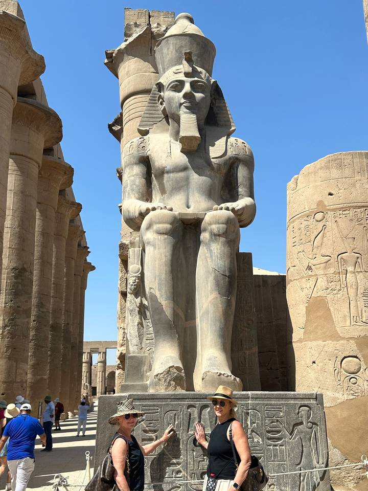 Une statue égyptienne antique et des colonnes couvertes de hiéroglyphes sous un ciel bleu.