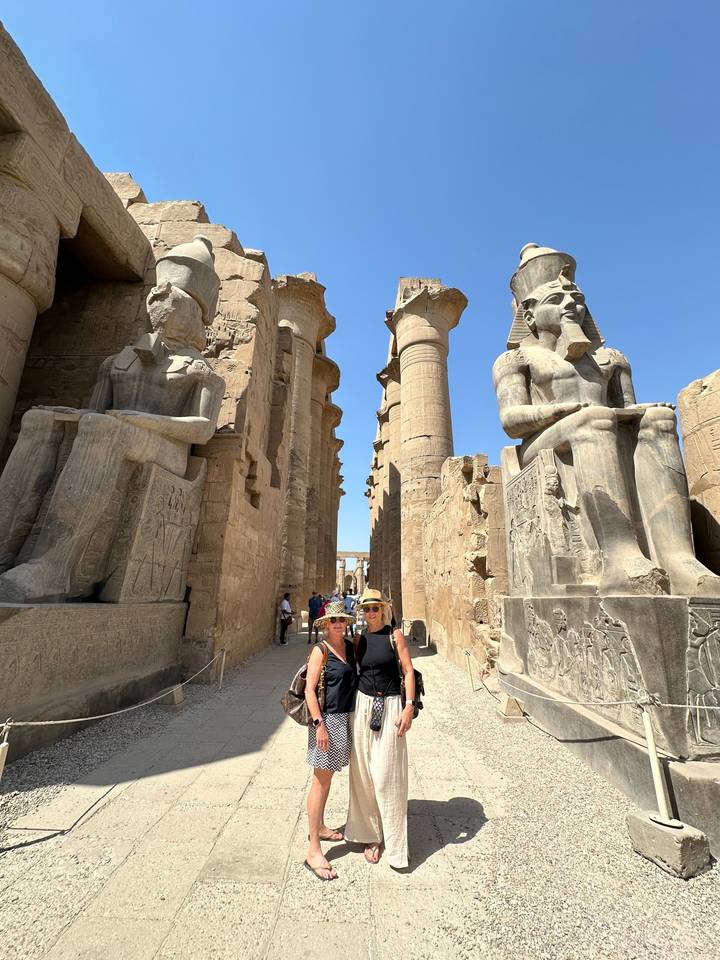 Deux personnes posant devant de grandes statues et colonnes sur un site historique.